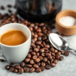 Xícara de café espresso com grãos de café e colher ao lado.